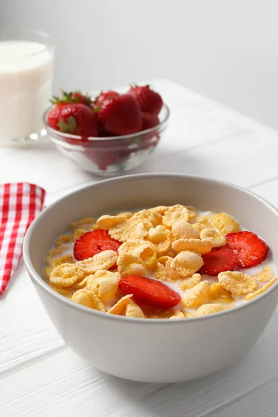 Corn flakes with strawberries in bowl served on white wooden table