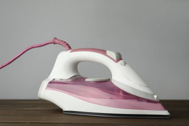 Açık gri arka plana karşı ahşap masa üzerinde modern bir ütü. Ev aletleri