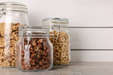 Beyaz ahşap duvarın yanındaki gri tezgahta farklı kahvaltı gevrekleri olan cam kaplar. Metin için boşluk