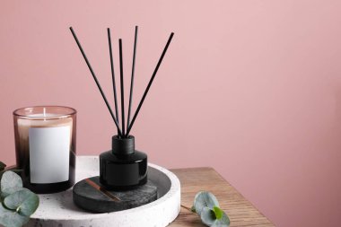 Pembe duvarın yanındaki ahşap masa üzerinde aromatik kamış oda spreyi ile kompozisyon, metin için boşluk