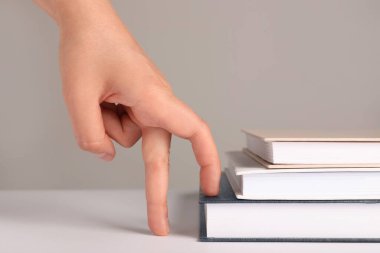 Woman imitating stepping up on books with her fingers against grey background, closeup