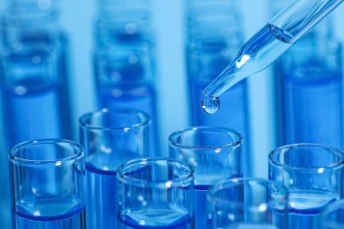 Açık mavi arkaplanda test tüpüne reaktör damlatılıyor, yakın plan ve metin için boşluk. Laboratuvar analizi