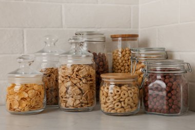 Tuğla duvarın yanındaki beyaz tezgahta farklı kahvaltı gevrekleri olan cam kaplar.