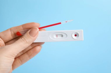 Elinde hepatit ve pipet için açık mavi arka planda kan olan tek kullanımlık ekspres test yapan bir kadın var.