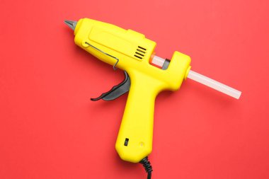 Sarı yapıştırıcı tabancası, kırmızı arka planda, üst görünümde.