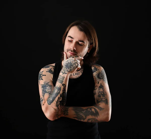 Young man with tattoos on body against black background