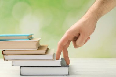 Man climbing up stairs of books with fingers on white wooden table against blurred background, closeup