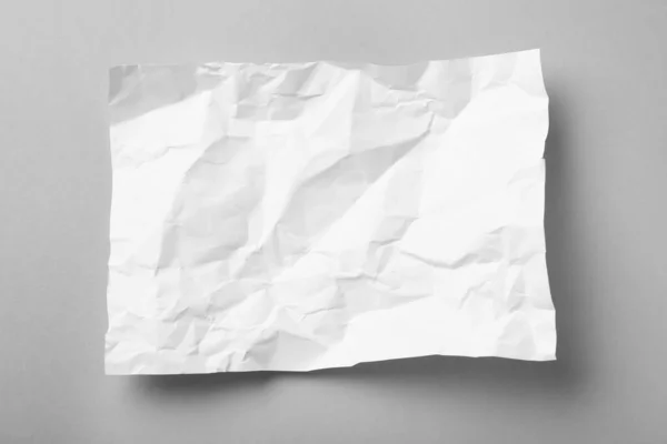 Sheet of white crumpled paper on grey background, top view