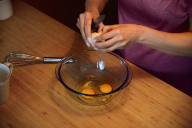 Krep hamuru için yumurta kıran kadın cam kasede, ahşap masada, yakın plan.