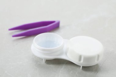 Case with contact lenses and tweezers on light grey table, closeup