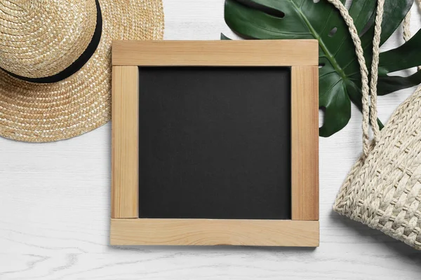 Blank chalkboard with stylish accessories and green leaf on white wooden table, flat lay. Space for text