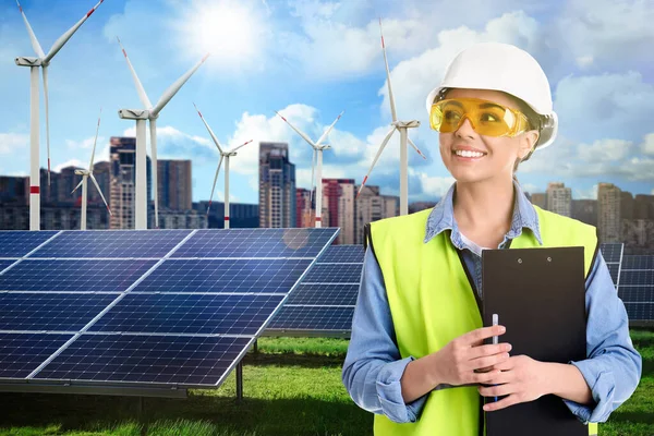 Industrial engineer in uniform and view of solar panels and wind energy turbines installed outdoors