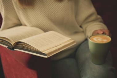 Elinde kahve fincanı olan kadın kitap okuyor, yakın plan.