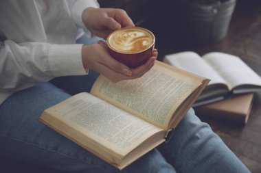 Elinde kahve fincanı olan kadın kitap okuyor, yakın plan.