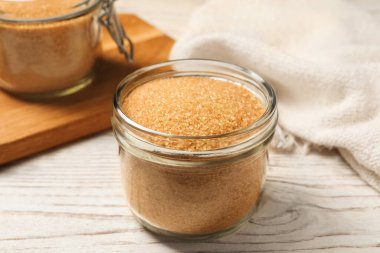 Kahverengi şekerli cam kavanoz beyaz ahşap masa, yakın plan.