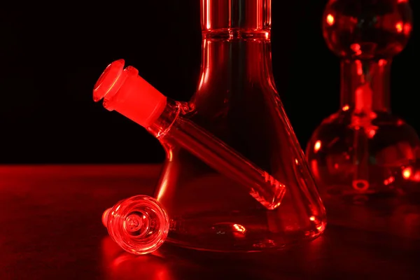玻璃瓶放在桌子上 黑色背景 红色调 吸烟装置 — 图库照片