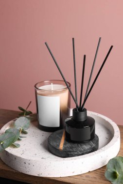 Pembe duvarın yanındaki ahşap masada aromatik kamış oda spreyi ile kompozisyon