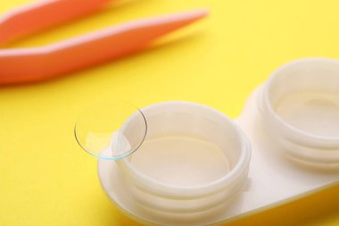 Sarı arkaplanda kontak lens ve cımbız kutusu, yakın plan