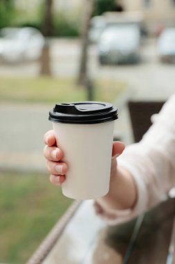 Woman holding paper takeaway cup at table outdoors, closeup. Coffee to go