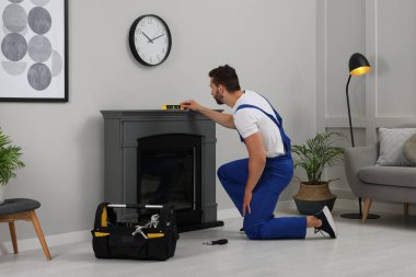 Professional technician using construction level for installing electric fireplace in room