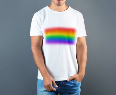 Gri arkaplanda LGBT gurur bayrağı resmi olan beyaz tişört giyen genç adam