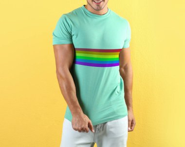 Sarı arka planda LGBT gurur bayrağı resmi olan turkuaz tişört giyen genç adam