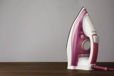 Açık gri arka plana karşı ahşap masa üzerinde modern bir ütü, yazı için yer. Ev aletleri