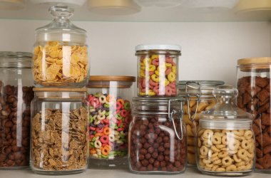 Rafta farklı kahvaltı gevrekleri olan cam kaplar.