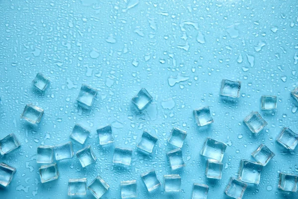 Ice cubes, water drops and space for text on turquoise background, flat lay. Refreshing drink ingredient