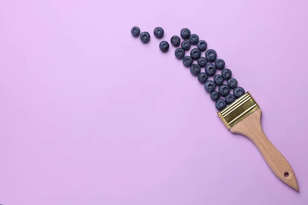 Creative flat lay composition with paint brush and blueberries on violet background. Space for text