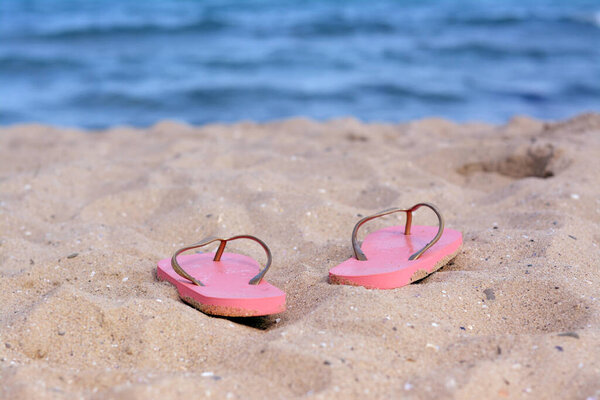 Stylish flip flops on sandy beach near sea