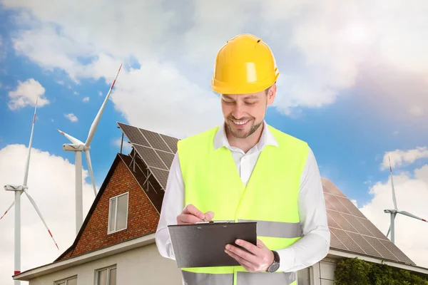 Ipari Mérnök Egyenruhában Kilátás Szélenergia Turbinák Közelében Ház Beépített Napelemek — Stock Fotó