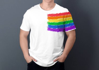 Gri arkaplanda LGBT gurur bayrağı resmi olan beyaz tişört giyen genç adam