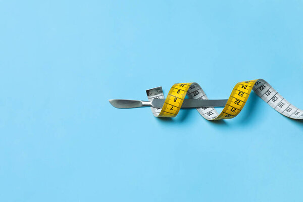 Scalpel and measuring tape on light blue background, top view with space for text. Weight loss surgery
