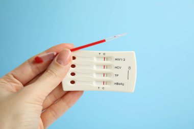 Elinde hepatit ve pipet için açık mavi arka planda kan olan tek kullanımlık ekspres test yapan bir kadın var.
