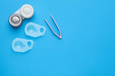 Açık mavi arka planda kontak lens ve cımbızlı çanta, düz konum. Metin için boşluk