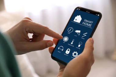 Smart Home uygulamasını kapalı mekanda cep telefonunda kullanan bir kadın.