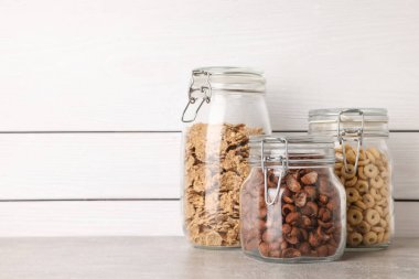 Glass containers with different breakfast cereals on grey countertop near white wooden wall. Space for text