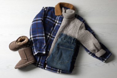 Sıcak çocuk kıyafetleri ve beyaz ahşap arka planda ayakkabılar.