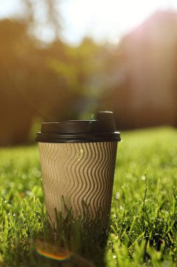 Yeşil çimlerin üzerinde plastik kapaklı karton kahve fincanı, mesaj için yer.