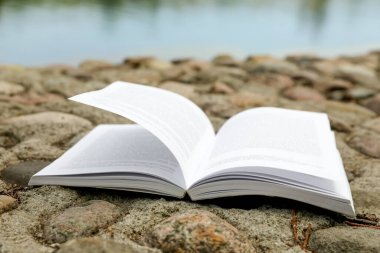 Open book on rocky shore near river