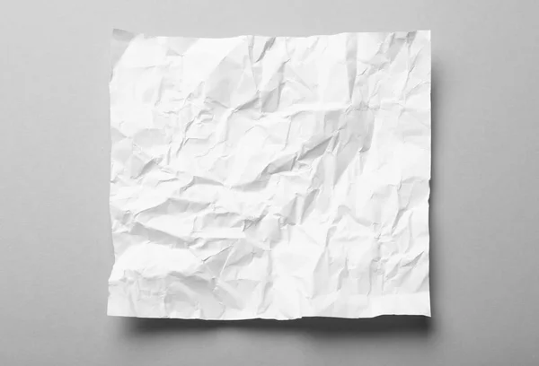 Sheet of white crumpled paper on grey background, top view