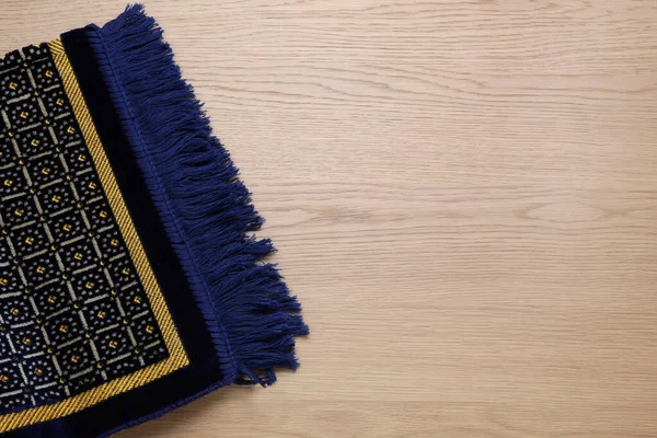 Muslim prayer rug on wooden table, top view. Space for text