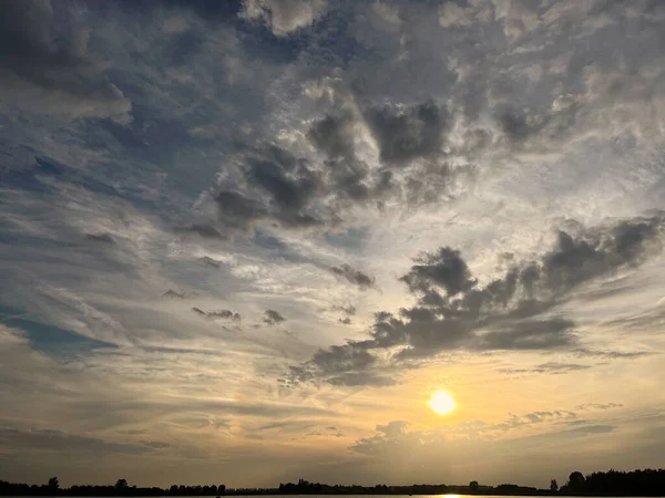 Sun in cloudy sky over lake during sunset