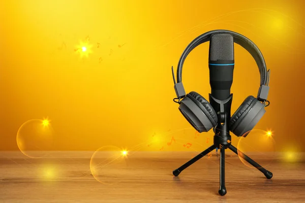 Modern headphones and microphone with illustration musical notes on wooden table against orange background. Space for text