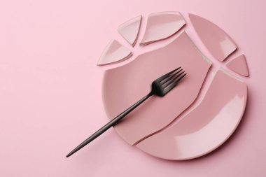 Kırık seramik plaka parçaları ve pembe arka planda çatal, düz. Metin için boşluk