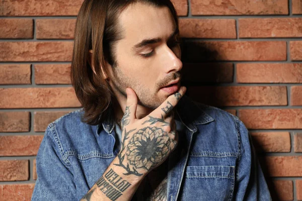 Young man with tattoos on hand near brick wall
