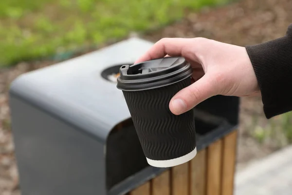 Man throwing black paper cup into trash can outdoors, closeup. Space for text
