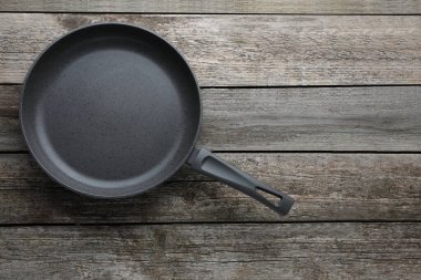 New non-stick frying pan on wooden table, top view. Space for text