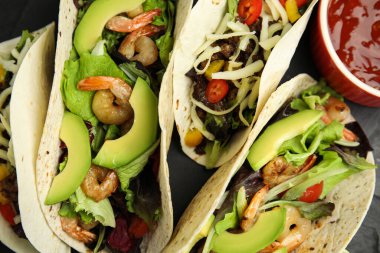 Lezzetli taco ve sos siyah masada, düz yerde.